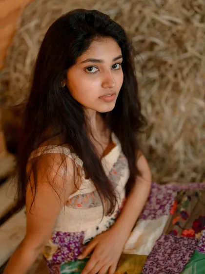 A soft and natural portrait of actress Rachana Inder. The rustic setting with hay bales provides a warm and earthy backdrop, creating a gentle and authentic feel.