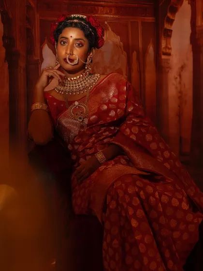 The lighting in this shot beautifully highlights the gold motifs on the red Banarsi saree, creating a warm, luxurious feel.