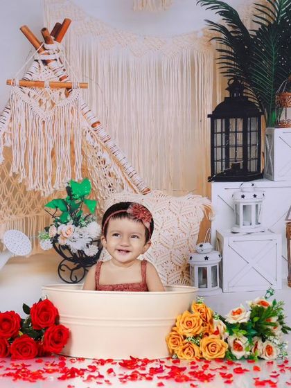 A boho-chic splash session featuring a baby in a tub surrounded by red roses and greenery. The macrame teepee and lanterns in the background create a stylish and trendy vibe.