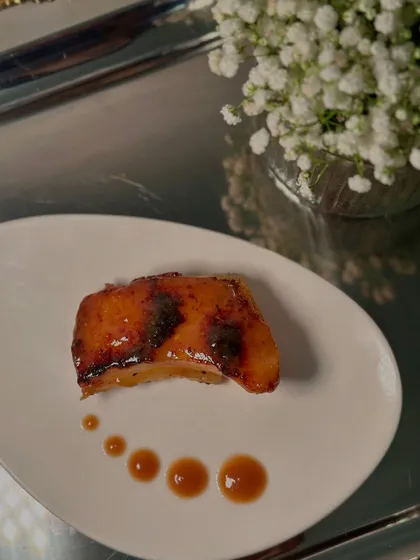 A perfectly seared piece of fish with a sweet and savoury glaze, dotted with sauce for an artistic presentation.