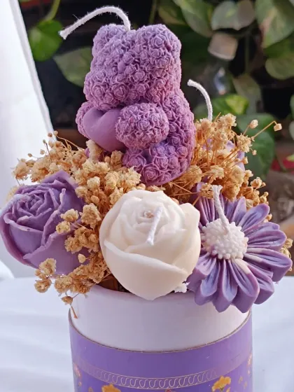A gift that truly blossoms. This flower bouquet candle features a purple teddy bear candle nestled among an arrangement of purple and white rose candles and dried flowers, all presented in a beautiful box.