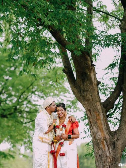 A tender moment under a large tree, with the groom kissing the bride's forehead.