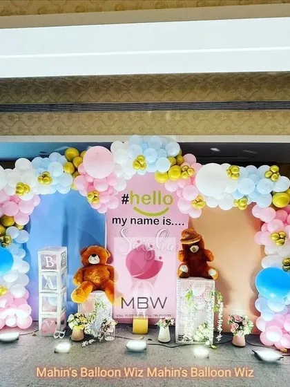 A "Hello My Name Is..." naming ceremony party with a teddy bear and hot-air balloon theme. The pink, blue, and gold balloon arch creates a festive and welcoming atmosphere.