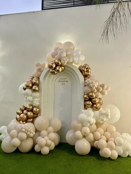 Elegance for a milestone celebration. This custom anniversary backdrop features a sophisticated organic balloon garland in nude, white, and chrome gold tones, creating a perfect photo opportunity for the happy couple.