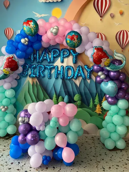 A beautiful mermaid-themed balloon arch in shades of aqua, purple, and pink, creating a magical underwater grotto for the birthday celebration.