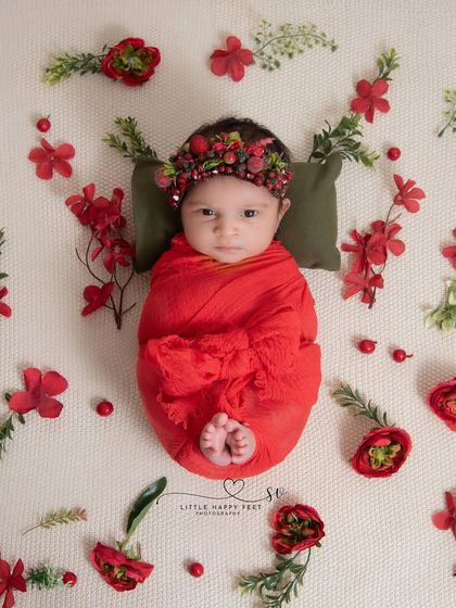 A beautiful flat-lay of a baby wrapped in red, surrounded by a pattern of red flowers. This is a modern and artistic approach to floral photography.