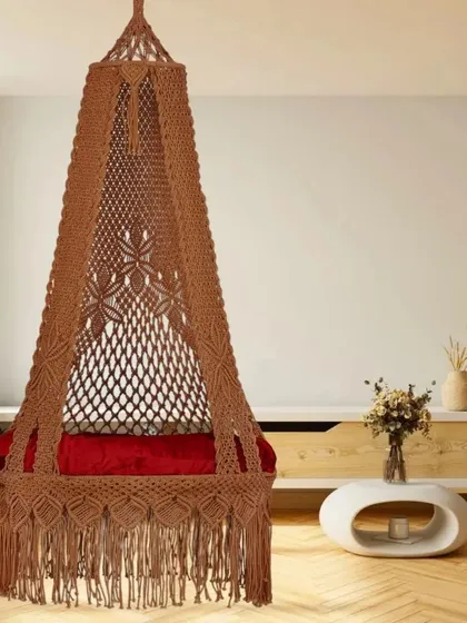 This single seater swing in a warm brown color is shown in a modern living room. The red cushion adds a vibrant pop of color to the earthy tones of the swing.