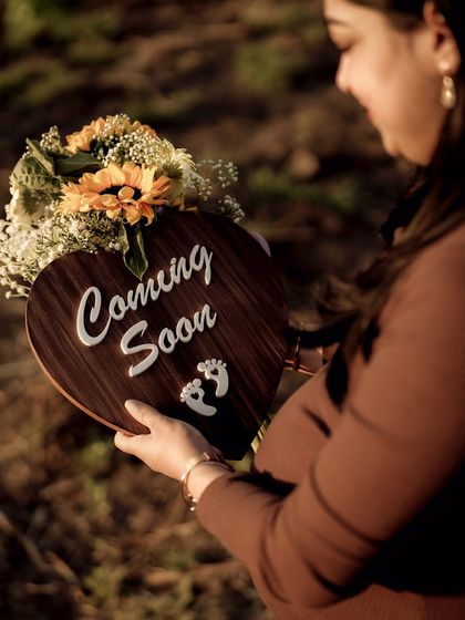 A beautiful, warm-toned photo of the mom-to-be holding a "Coming Soon" sign and a bouquet of sunflowers, embodying the glow of pregnancy.