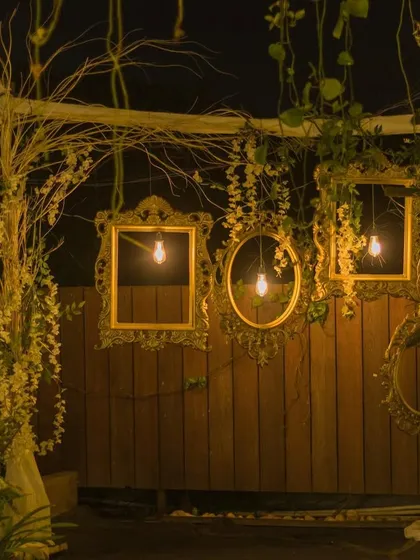 A rustic photo booth corner at night, featuring vintage frames, bare bulbs, and climbing vines for a charming, whimsical feel.