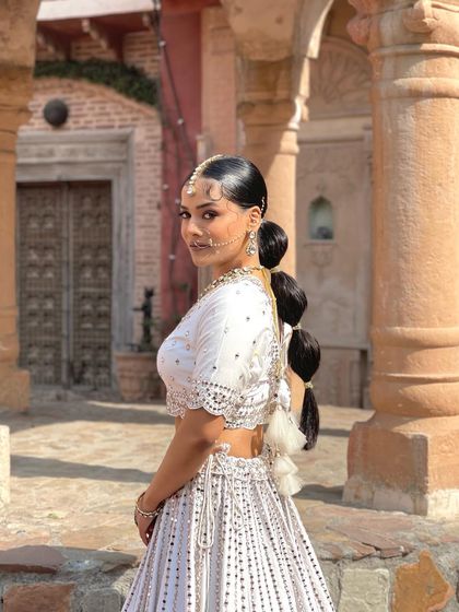A full view of the bride in her stunning white lehenga. The sleek bubble ponytail adds a touch of modern edge to her look.