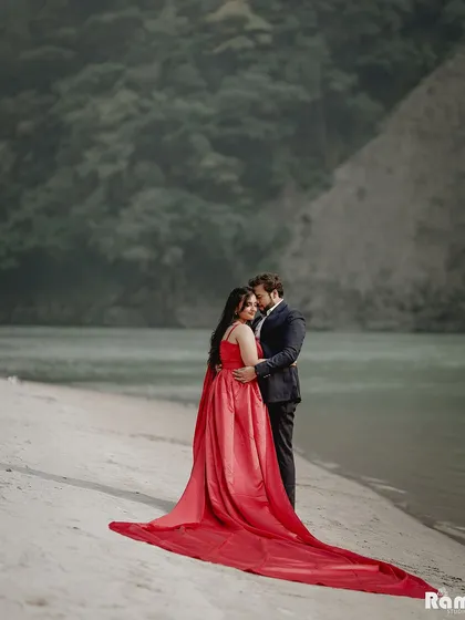 An intimate embrace by the river, with the bride's stunning red gown trailing behind her. The misty mountains in the background add to the serene and romantic mood of this destination shoot.
