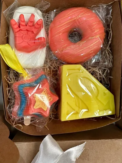 A close-up of a superhero soap box, containing an Iron Man popsicle, a donut soap, a Superman soap, and a star popsicle.