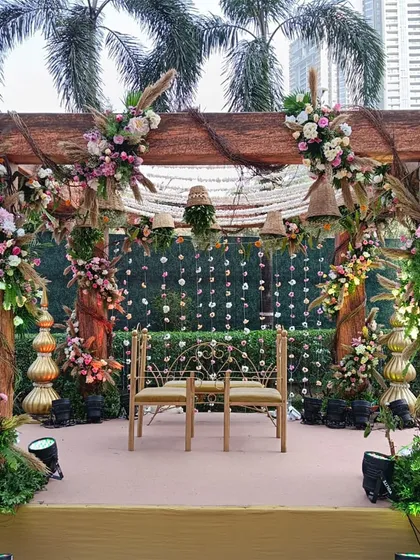 A front view of the rustic wooden mandap, showcasing the seating arrangement for the couple against a backdrop of hanging floral strings.