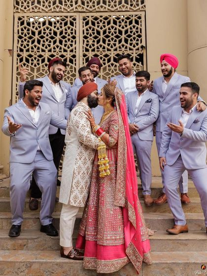 A fun and memorable shot of the couple sharing a kiss while the groomsmen cheer them on, adding a touch of modern fun to a traditional wedding day.