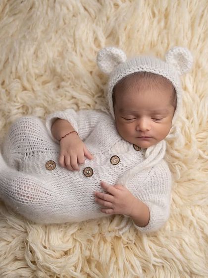 A side pose of the baby in the teddy bear outfit, sleeping on a soft fur rug. This highlights their tiny profile and curled-up posture.