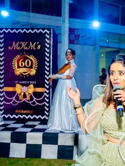 As your host and creative director, I'm right there on stage making sure everything runs smoothly. Here, I'm emceeing a 60th birthday bash, flanked by elegant violinists who welcomed the guests.