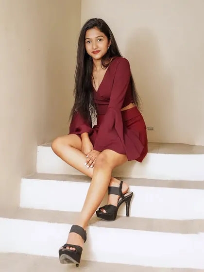 A relaxed and confident pose on a staircase, showcasing a stylish maroon co-ord set with bell sleeves and high heels.