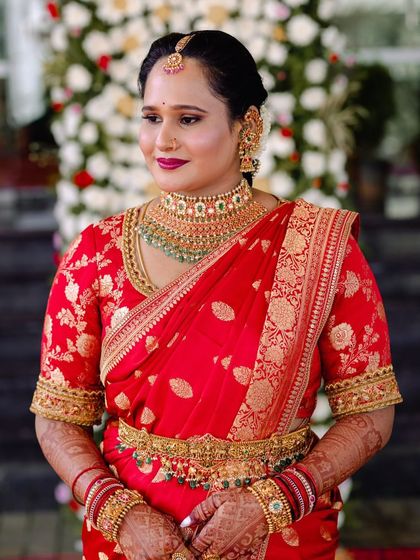 A bride in a vibrant red Banarasi silk saree. The blouse is embroidered with gold thread, matching the saree's intricate motifs.