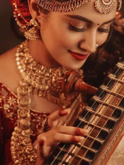 A close-up shot focusing on the bride's hands on the veena, highlighting the intricate henna and the beautiful details of the instrument. It's a celebration of art and tradition.