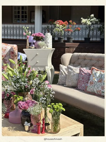 A beautiful outdoor lounge setting with a mix of floral-print and neutral-toned furniture, surrounded by an abundance of fresh flowers in various vases, creating a lush, garden-party feel.