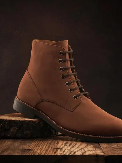 A hero shot of a single brown leather boot for Hanker. The rustic wood slice and dark, textured background create a rugged and timeless feel.