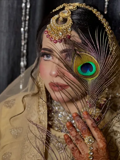 A creative and iconic shot, with the peacock feather partially covering the face. This highlights the eye makeup and creates a sense of mystery and allure.
