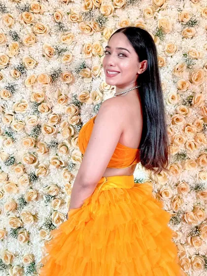 Blossom. A bright and happy picture in a beautiful orange lehenga against a wall of yellow roses.