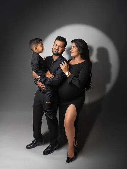 Celebrating the journey to parenthood with a classic, dramatic studio portrait. This maternity session uses a spotlight effect and coordinated black outfits to create a sophisticated and timeless family photograph.