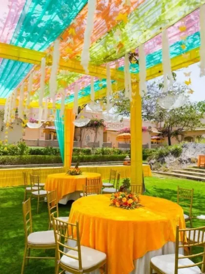 A beautiful outdoor seating arrangement for a Haldi lunch. The pastel-colored canopy with hanging butterfly cutouts adds a whimsical touch to the decor.