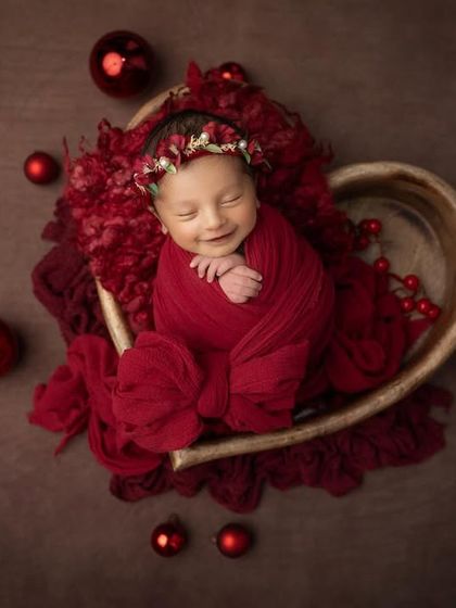 Another angle of this joyful Christmas baby, showing her sweet smile and cozy red wrap. These holiday themed sessions are a wonderful way to create memories for your family's greeting cards.