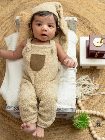 This little one is awake and curious in his adorable bear outfit. The setup includes a miniature bed and vintage gramophone for a touch of rustic charm.