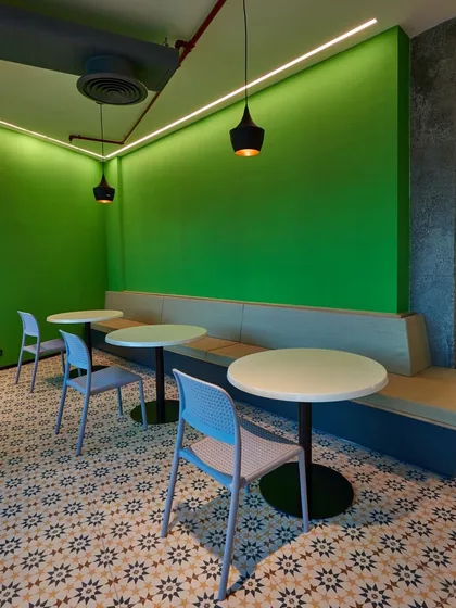 A simple yet inviting cafe nook with a bright green accent wall, built-in banquette seating, and patterned floor tiles.