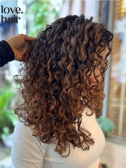 A side profile showing how the balayage highlights weave through the curls, creating depth and movement. This is a great option for a natural, sun kissed effect.