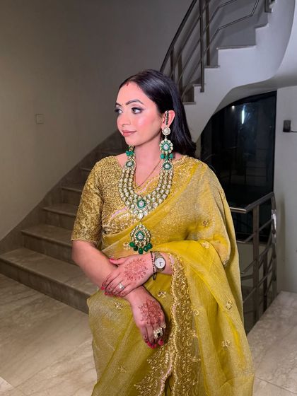 A stunning guest look featuring a beautiful yellow saree and statement emerald jewelry. The makeup is kept classic to balance the look.