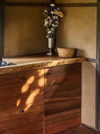 The kitchenette in the prefab cottage, featuring a live-edge wooden countertop and cabinets set against the textured earthen walls.