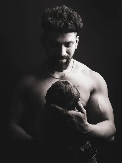 A dramatic black and white photo of a father holding his newborn. The lighting is carefully controlled to create a powerful and emotional image that emphasizes the father's protective embrace.