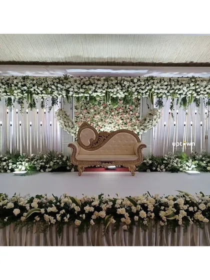 For engagements and receptions, I create sophisticated floral backdrops. This elegant white-on-white stage design uses a dense wall of flowers and a classic chaise lounge to create a timeless and romantic setting for the couple.