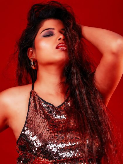 A glamorous close-up with a focus on the glittery makeup and confident expression. The red light adds warmth and intensity.