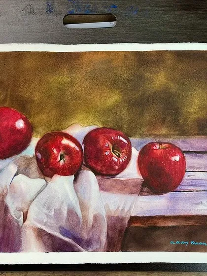 The apple still life on my desk, showing the finished painting next to the watercolor palette.