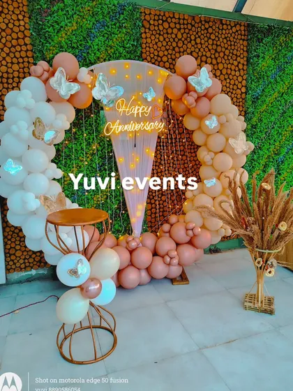 A whimsical anniversary backdrop featuring a circular balloon arch in pastel pinks and whites. I added butterfly cutouts and a 'Happy Anniversary' neon sign to create a soft, romantic theme for the celebration.