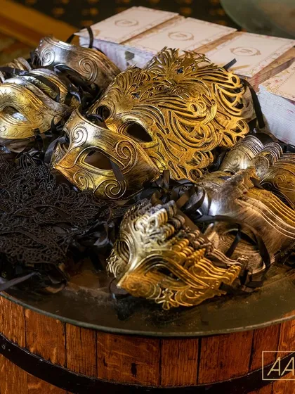 As part of a speakeasy-themed cocktail party, guests were invited to choose a mask for the masquerade. These ornate gold, silver, and black lace masks were presented on a rustic wooden barrel, serving as both a party favor and an invitation to join the night's mystery.