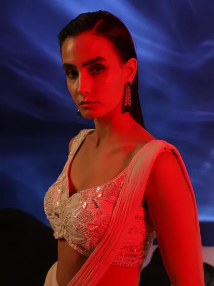 An intense, close-up shot with dramatic red lighting. The focus is on the model's expression and the intricate beadwork of the blouse, creating a powerful and emotional image.