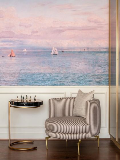This serene reading corner is set against a custom mural depicting a calm seascape. The striped armchair and elegant side table create a perfect spot to get lost in a good book.