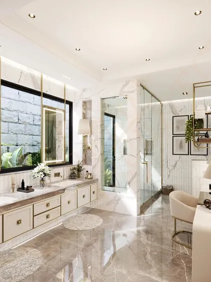 A bright and airy luxury bathroom clad in white marble, featuring a double vanity, a dedicated dressing table, and large windows that overlook a private garden.
