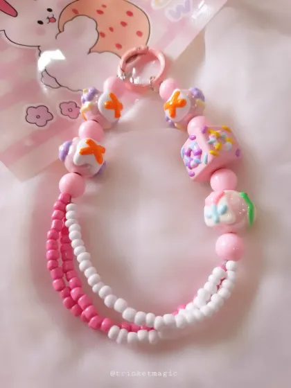 This adorable pink and white beaded charm is perfect for your phone or bag. It features intricate candy-like beads and a double-strand design for a playful, textured look.