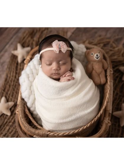 A beautiful overhead shot of a sleeping baby girl, snugly wrapped in a basket. The rustic textures of the basket and mat contrast beautifully with the soft white wrap and fabric stars, creating a lovely composition.