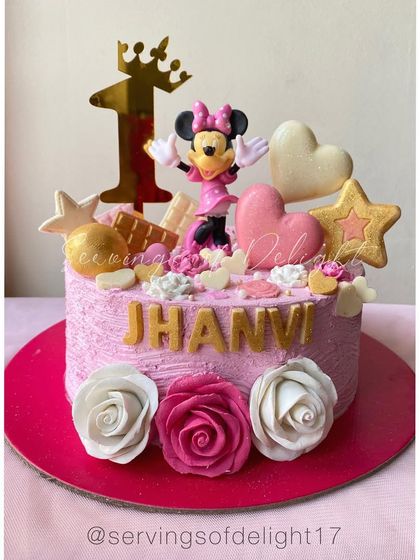 A pretty-in-pink Minnie Mouse cake for a first birthday. It's decorated with fondant roses, stars, and a golden "one" topper.