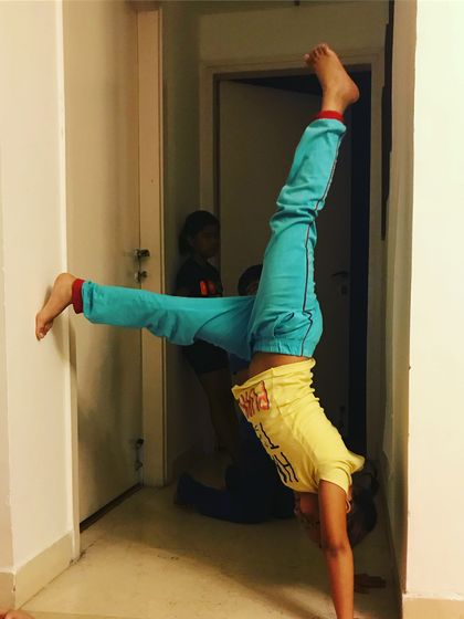 Practice makes progress. This child is working on her handstand with a split leg variation, showing how we can add creative and fun challenges as they get stronger.