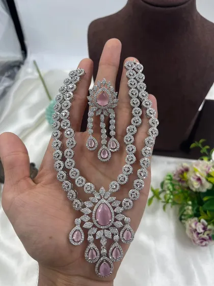 A hand-held view of the layered AD necklace with a pink stone.