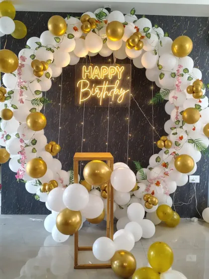 This elegant birthday backdrop is one of my most popular designs. It features a large circular frame decorated with white and gold balloons, delicate artificial leaves, and a central 'Happy Birthday' neon sign, perfect for photos.